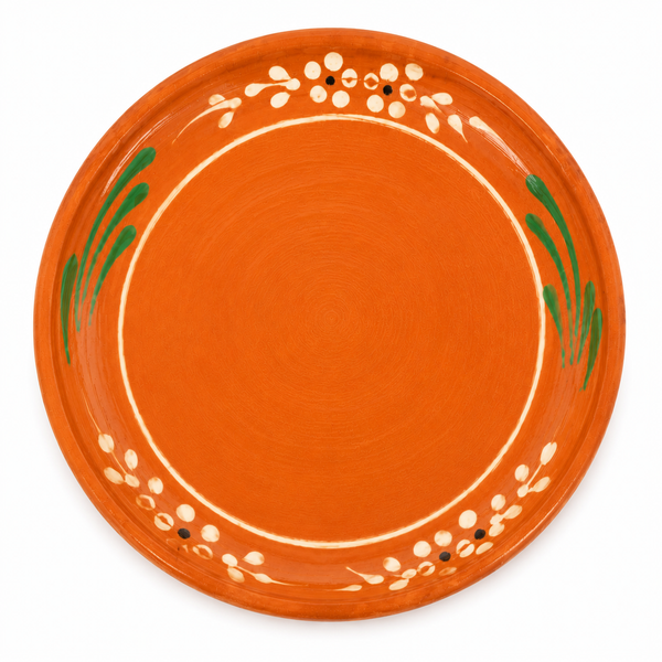 An orange ceramic plate with hand-painted green leaf motifs and white floral accents around the rim, shown from a top-down view on a white background.