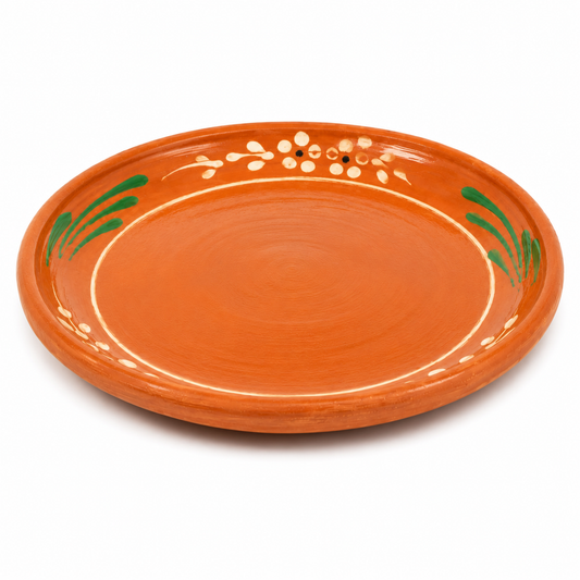 An orange terracotta ceramic serving platter with hand-painted green leaf motifs and white decorative details on the rim, shown on a white background.